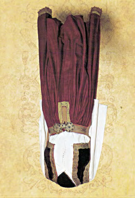 Jeleku është i punuar nga kadifeja e kuqe e mbyllur dhe e zbukuruar me shirita ari në skaje. Këmisha, e bardhë e pambuktë, e zbukuruar me dantelë të punuar në dorë reth qafës dhe skajeve e mëngëve.