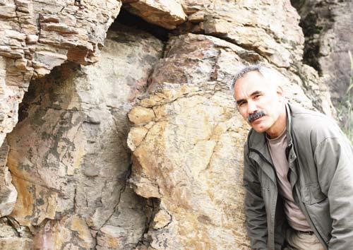 Mustafa Aksoy araştırma alnında bir kayada dövme tekniği ile yapılmış resimler önünde lan damgalar ile şekiller olmuştu.