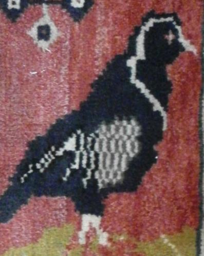 Halının zemininde hardal renk hakimdir ve siyah, kahverengi, gri, sarı ve kırmızı renklerden oluşan ve birbirine bakan tasvir edilmiş iki güvercin motifi göze çarpmaktadır.