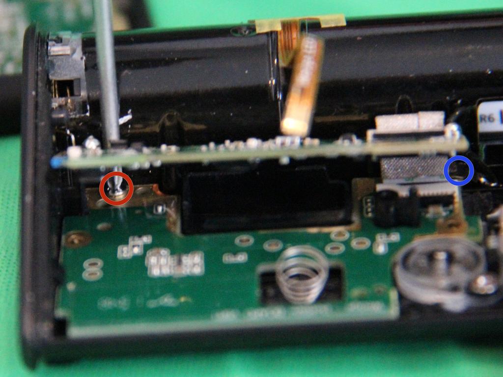 Küçük bir Phillips üst PCB ve kırmızı daire vidayı çıkarmak için pil bölmesi arasına tornavida kaydırın.